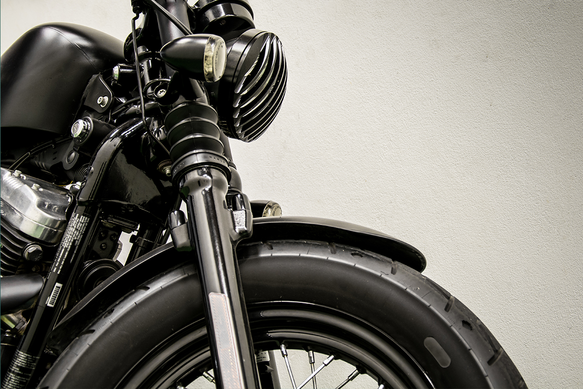 Close-up of the front wheel, fork, and headlight of a black motorcycle against a light gray background. Close-up of the front wheel, fork, and headlight of a black motorcycle against a light gray background.